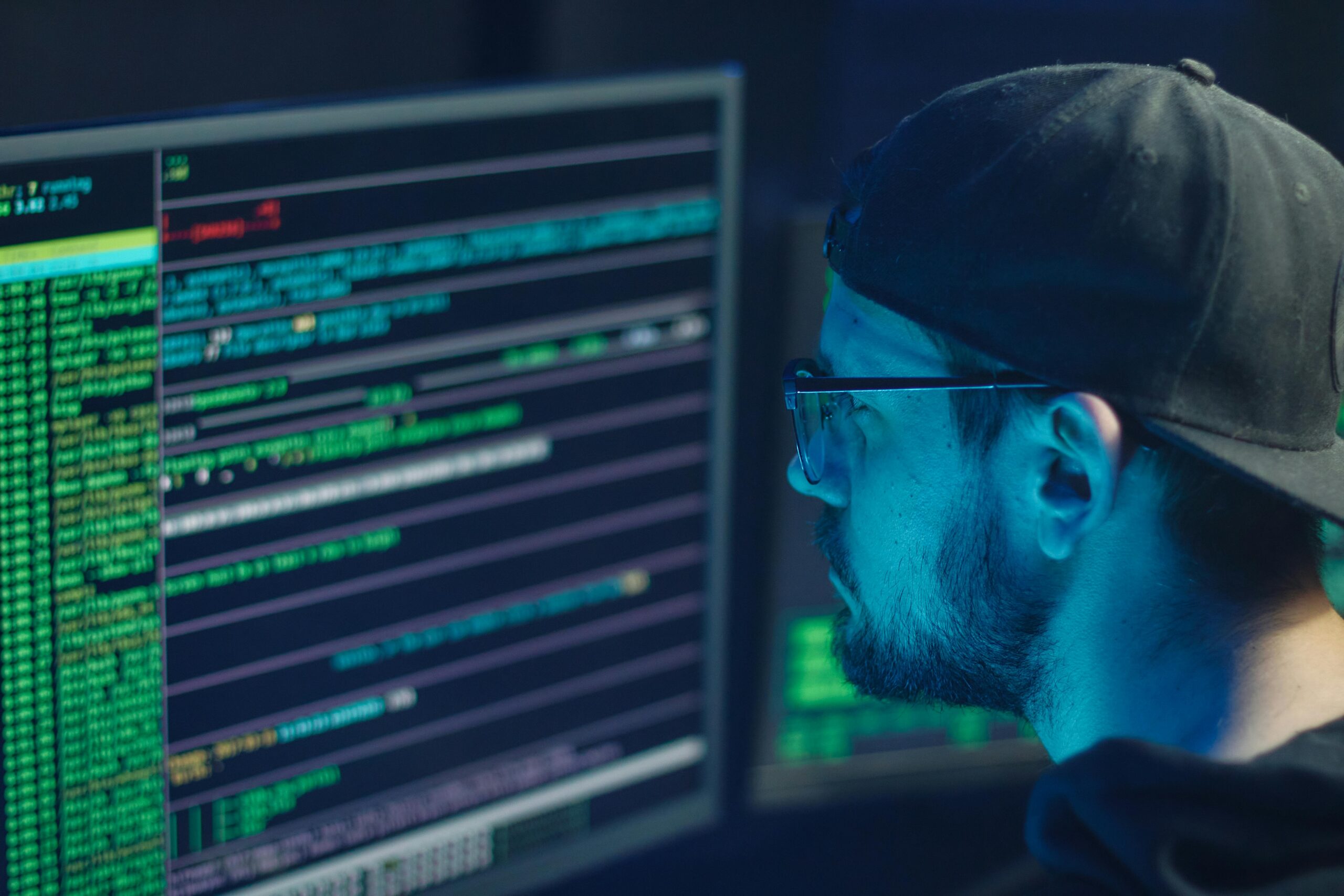 man in a hat and glasses coding on a computer 