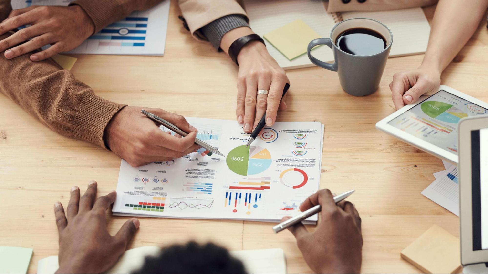 Three people in a meeting looking at a document with graphs and rates  
